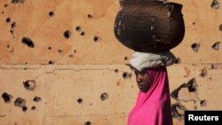 A girl walks by a building pockmarked with bullet holes from fighting in Gao, Mali, Mar. 13 2013. 