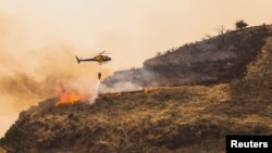 Sebuah helikopter menyiramkan air dalam upaya memadamkan kebakaran hutan yang melanda desa Valleseco, Gran Canaria, Kepulauan Canary, Spanyol, 17 Agustus 2019. (REUTERS / Borja Suarez)