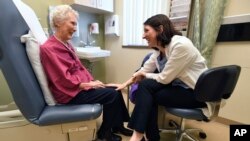 In this March 4, 2019 photo, Dr. Allison Magnuson, left, speaks with patient Nancy Simpson at the Pluta Cancer Center in Rochester, N.Y.