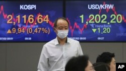 A currency trader passes by screens showing Korea Composite Stock Price Index (KOSPI), left, and foreign exchange rate at the foreign exchange dealing room of the KEB Hana Bank headquarters in Seoul, South Korea, July 2, 2020.