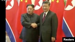 Pemimpin Korea Utara Kim Jong Un berjabat tangan dengan Presiden China Xi Jinping, dalam foto yang diambil dari rekaman video yang dirilis 28 Maret 2018. 