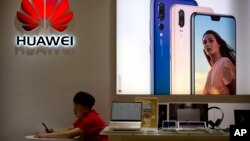 FILE - A sales clerk looks at his smartphone in a Huawei store at a shopping mall in Beijing Wednesday, July 4, 2018. 
