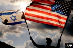 Seorang pengunjuk rasa mengibarkan bendera nasional AS dan Israel saat demonstrasi di depan kedutaan AS di Tel Aviv, saat Perdana Menteri Israel Benjamin Netanyahu berada di New York untuk bertemu Presiden Joe Biden, pada 20 September 2023. (Foto: AFP