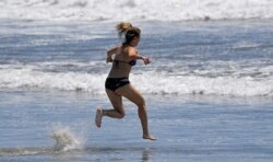 A swimmer runs into the ocean at Venice Beach during the coronavirus outbreak, May 13, 2020, in Los Angeles.