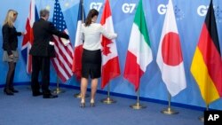 Workers adjust the flags of a Group of Seven meeting in Brussels, Belgium, June 5, 2014. G-7 foreign ministers are meeting Monday and Tuesday in Tuscany, Italy.