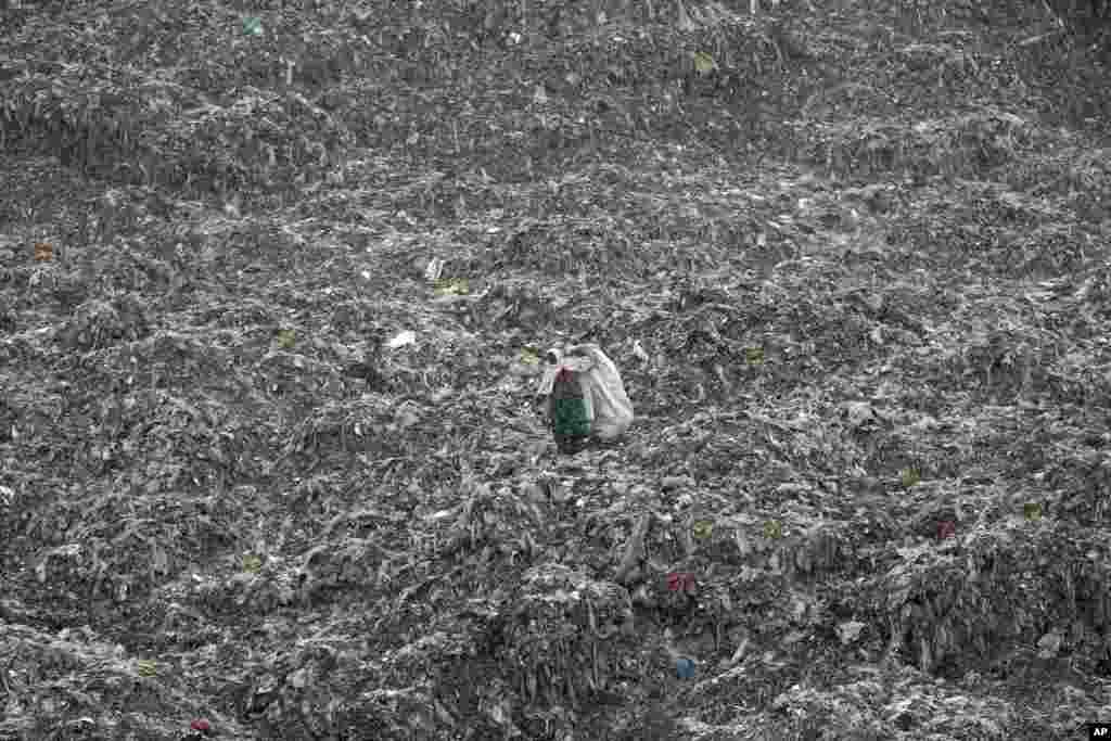 FILE - A woman who scavenges recyclable materials from garbage for a living walks across a mountain of garbage at the dump on the outskirts of Kabul, Afghanistan, Dec. 11, 2018.