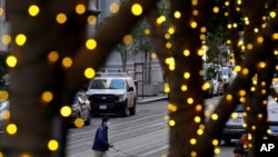 Holiday lights line trees as people wearing face masks cross an intersection during the coronavirus pandemic in San Francisco, Dec. 17, 2020. 