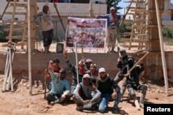 Members of "You Destroy and We Rebuild Brigade" pose at a construction site in front of their banner depicting a still from their parody video that circulated on Syrian social media, in the rebel-held town of Saida, in Deraa province, Syria, May 24, 2017.