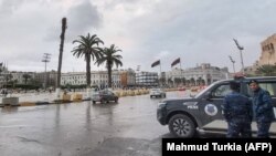 Des policiers se tiennent près d'un véhicule de patrouille sur la place des Martyrs de Tripoli, la capitale de la Libye, le 13 décembre 2021.