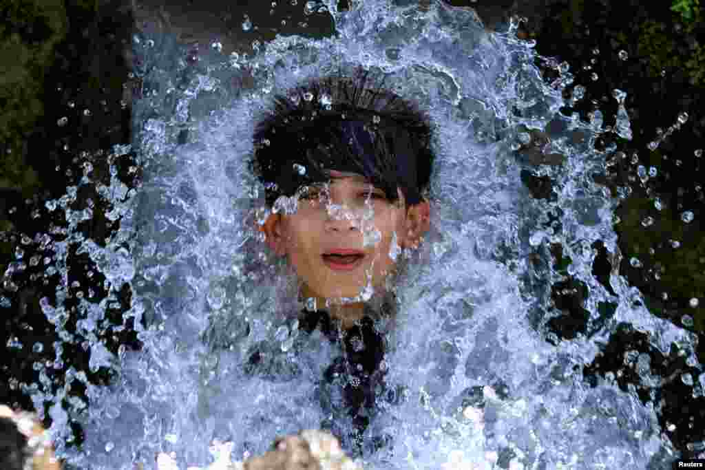 A boy holds his head against a water pipe from a canal on a hot day on the outskirts of Peshawar, Pakistan.