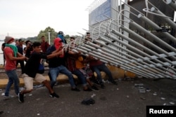 FILE - A group of men part of a caravan of thousands of migrants from Central America en route to the U.S, pull down the border gate with the intention to carry on their journey, in Tecun Uman, Guatemala, Oct. 28, 2018.