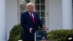 Presiden Donald Trump meraih sebuah kotak berisi tes cepat COVID-19 dari Abbott Laboratories, di Gedung Putih, Senin, 30 Maret 2020, di Washington. (Foto: AP / Alex Brandon)