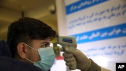 FILE - An Afghan health worker takes the temperature of a passenger as a preventive measure for Coronavirus, during screening of travelers who arrived from China, at the Hamid Karzai International Airport in Kabul, Feb. 3, 2020.