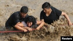 Rescuers help people cross a flooded street after a massive landslide and flood in the Huachipa district of Lima, Peru, March 17, 2017. 