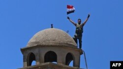 FILE - A Syrian soldier waves the national flag atop the Greek Orthodox Church of St. George in the town of Quneitra in the Syrian Golan Heights, July 27, 2018.