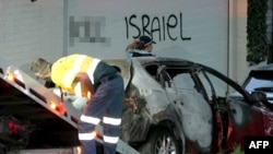 Cuplikan bingkai dari video Australian Broadcast Corporation 11 Desember 2024, menunjukkan seorang polisi berjalan melewati mobil yang dibakar dan sedang disingkirkan dari depan grafiti anti-Israel di dinding di pinggiran kota Sydney (gambar sebagian diburamkan oleh VOA).