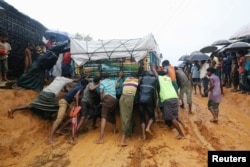 Rohingya refugees pushing a truck that is stuck in mud after heavy rain at Kutupalong camp in Cox's Bazar, Bangladesh, July 4, 2018.