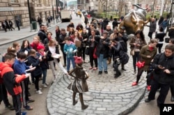 A crowd gathers around a statue of a fearless girl facing the Wall Street Bull, Wednesday, March 8, 2017, in New York.