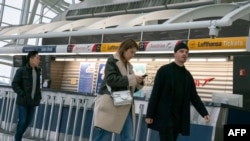 Orang-orang berjalan melintas di depan gerai maskapai penerbangan Jerman, Lufthansa, di Terminal 1, Bandara Internasional John F. Kennedy, di New York, 12 Maret 2020. (Foto: Kena Betancur/AFP)