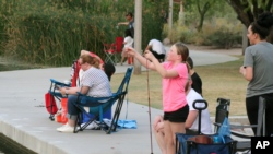 FILE - A girl checks her line as people fish at Veterans Oasis Park in Chandler, Arizona, April 30, 2020, a popular activity in some areas during the coronavirus pandemic.