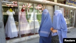 FILE - Afghan women walk past a shop specialising in wedding dresses in Kabul.