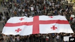 Georgian demonstrators carry a state flag during a protest rally against prison abuse in Tbilisi, Georgia, Sept. 20, 2012