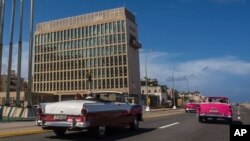 Para wisatawan mengendarai mobil klasik melintas gedung Kedubes AS di Havana, Kuba, 3 Oktober 2017.