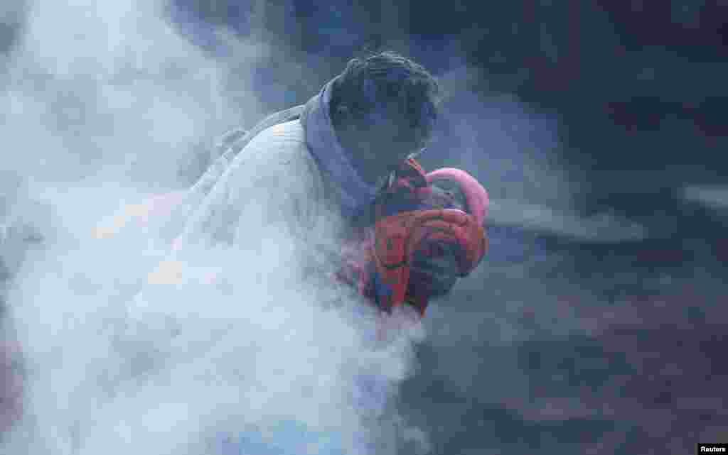 បុរស​ម្នាក់​បី​ទារក​ម្នាក់​នៅ​ជិតភ្នក់​ភ្លើង​មួយ​នាពេលព្រឹក​ព្រហាមដ៏ត្រជាក់​ក្នុង​ទីក្រុង​ញូវដែលី​ប្រទេស​ឥណ្ឌា។