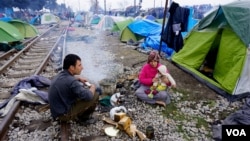 Refugee family attempts to stay warm along Macedonia-bound railroad tracks, Idomeni, Greece, March 16, 2016. (J. Dettmer/VOA)