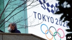 Seorang pria mengenakan masker untuk mencegah penularan virus corona berjalan dekat spanduk Olimpiade Tokyo 2020, 25 Februari 2021. (Foto: AP)