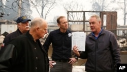 California Gov. Jerry Brown, second from left, looks at a students work book displayed by Interior Secretary Ryan Zinke, that was found during a tour of the fire ravaged Paradise Elementary School Wednesday, Nov. 14, 2018, in Paradise, Calif. 