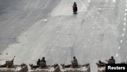Two men on a scooter ride near soldiers on military vehicles at Abbasiya square near Egypt's Defence Ministry, in Cairo, May 4, 2012. 