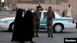 Wasu mata suna tafiya a titi akan Titi a Saudiyya yayin da wasu jami'an tsaro ke tsaye a gefe, ranar 14, ga watan Nuwamba, 2013.