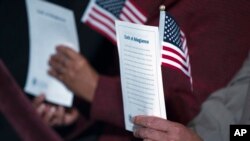 FILE - Participants hold the "Oath of Allegiance" and American flags during a naturalization ceremony at the National Archives in Washington, Dec. 15, 2015.