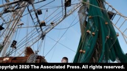 Minh Nguyen, wearing a mask out of fear of the catching the coronavirus, cleans his shrimp boat in Morgan City, La. Monday, May 11, 2020. 