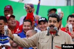 FILE - Venezuela's President Nicolas Maduro holds up a mock 100-bolivar bill depicting the president of the National Assembly Henry Ramos Allup, during a pro-government rally in Caracas, Dec. 17, 2016.