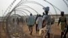 FILE - Displaced people walking next to a razor wire fence at the United Nations base in the capital Juba, South Sudan. 