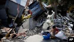 A boy sits with items salvaged from the ruins of a house in the Balaroa neighborhood in Palu, Central Sulawesi, Indonesia, Oct. 2, 2018. 