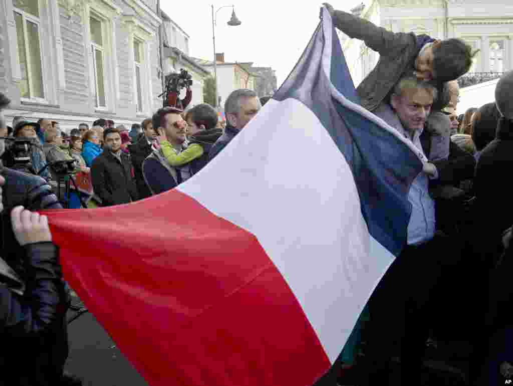 Warga memegang bendera Perancis sambil menunggu upacara penghormatan untuk para korban serangan maut Paris, di Kedutaan Besar Perancis di Bukares, Rumania (15/11). (AP/Vadim Ghirda)