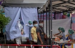 Muaythai boxing fighters and officials gather at a makeshift screening facility as a man in a Hazmat suite talks with a nurse outside Rajadamnern boxing stadium in Bangkok, Thailand, Thursday, March 19, 2020.