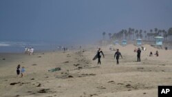 Two surfers walk to the water, May 1, 2020, in Huntington Beach, Calif. California Gov. Gavin Newsom ordered all Orange County beaches closed starting Friday after thousands gathered last weekend in Huntington Beach and Newport Beach.