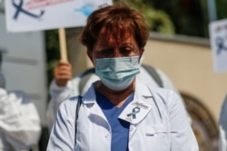 A health worker wearing a face mask to help prevent the spread of the coronavirus wears and a picture of a black ribbon to raise concerns over COVID-19 deaths and increasing numbers of patients, Istanbul, Sept. 15, 2020.
