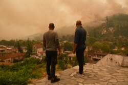 Penduduk setempat menyaksikan kebakaran yang membumi hanguskan desa Gouves, di pulau Evia, Yunani, 8 Agustus 2021. (REUTERS/Alexandros Avramidis)