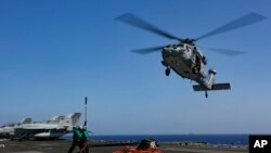 FILE - In this Friday, May 10, 2019, photo released by the U.S. Navy, logistics specialists prepare to attach cargo to an MH-60S Sea Hawk helicopter on the flight deck the Nimitz-class aircraft carrier USS Abraham Lincoln in the Persian Gulf.