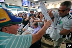 Venezuelans vie for T-shirts as they watch televised news from their country at the El Arepazo Doral Venezuelan restaurant in Doral, Fla., April 30, 2019.