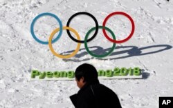 FILE - A man walks by the Olympic rings with a sign of 2018 Pyeongchang Olympic Winter Games, in Pyeongchang, South Korea, Feb. 3, 2017.