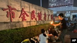 A woman lights a candle near flowers placed outside the Zhuhai People's Fitness Plaza where a man deliberately rammed his car into people exercising at the sports center, in Zhuhai in southern China's Guangdong province, Nov. 12, 2024.