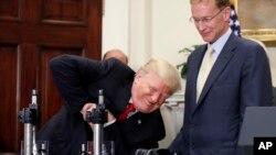 FILE - President Donald Trump unsuccessfully attempts to crush a Corning Valor glass protective vial with Wendell P. Weeks, right, chairman and chief executive officer of Corning Glass, in the Roosevelt Room of the White House, July 20, 2017.