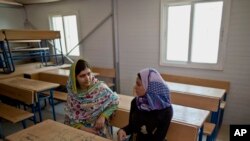 FILE - Nobel Peace Prize laureate Malala Yousafzai, 18, left, and Mezon al-Melihan, a 17-year-old refugee from the southern Syrian town of Deraa, talk while visiting a class at Azraq refugee camp, Jordan, July 13, 2015. 