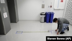 Kevin Gonzales, director of operations at the Rajen Kilachand Center for Integrated Life Sciences and Engineering, at Boston University, places safe distancing floor markings near an elevator on the school's campus, in Boston, Thursday, May 21, 2020. (AP Photo/Steven Senne)